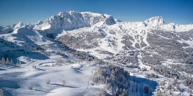 Snow-covered mountain landscape with ski slopes and a forested valley under a clear sky