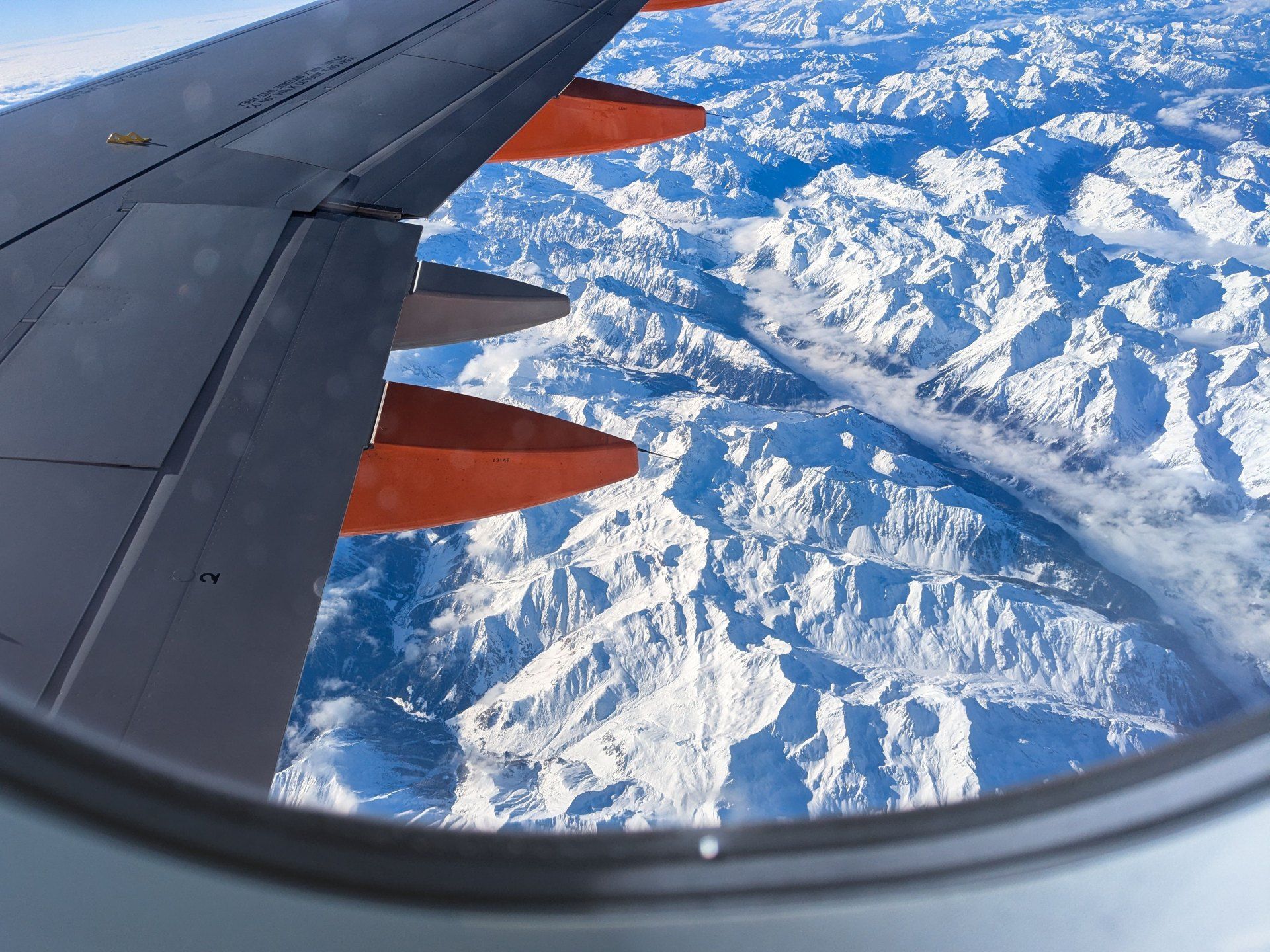 Airplane wing over snowy mountain landscape seen from a window