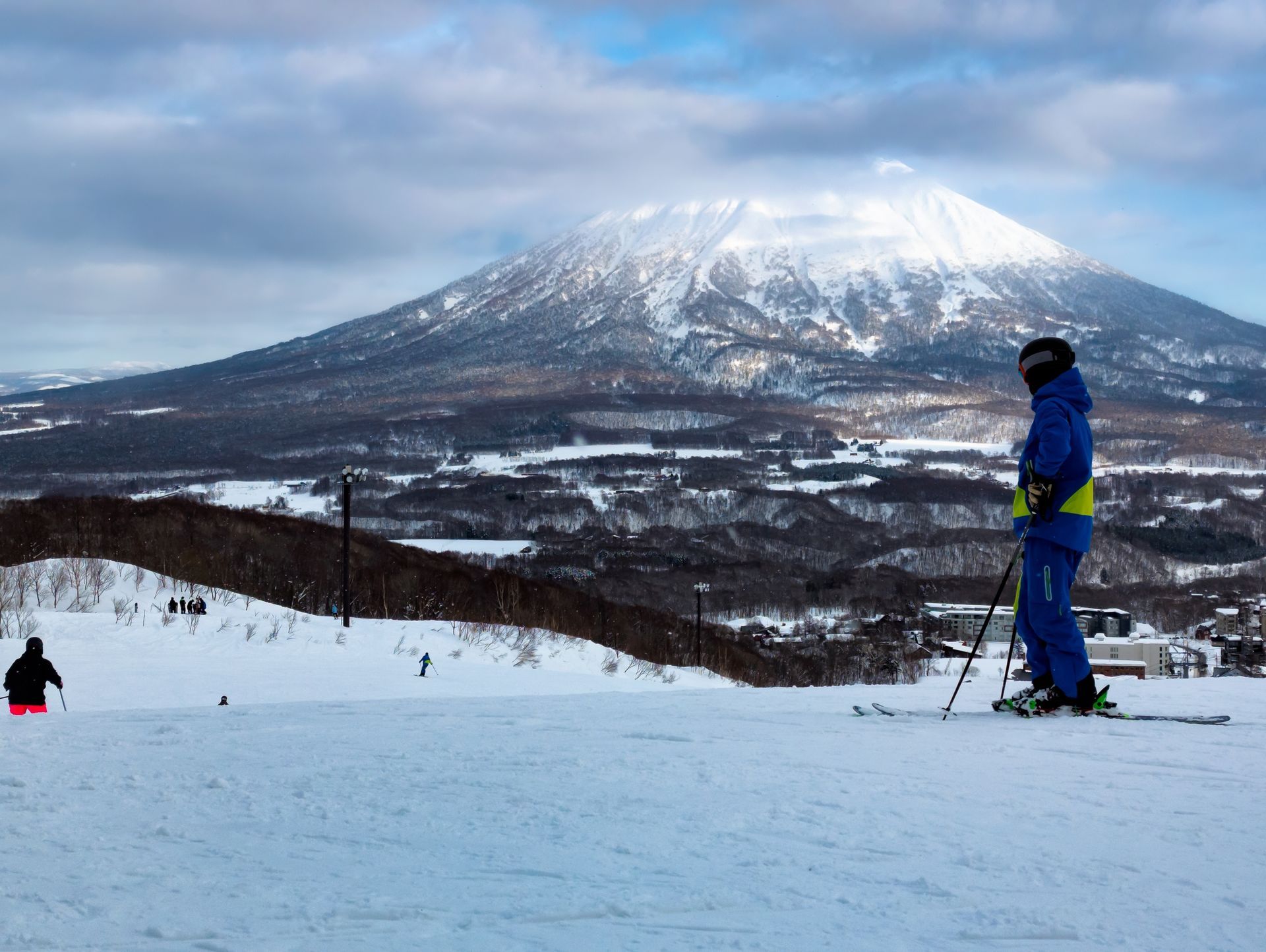 Skier in blue on a snowy slope with a large snow-covered mountain in the background