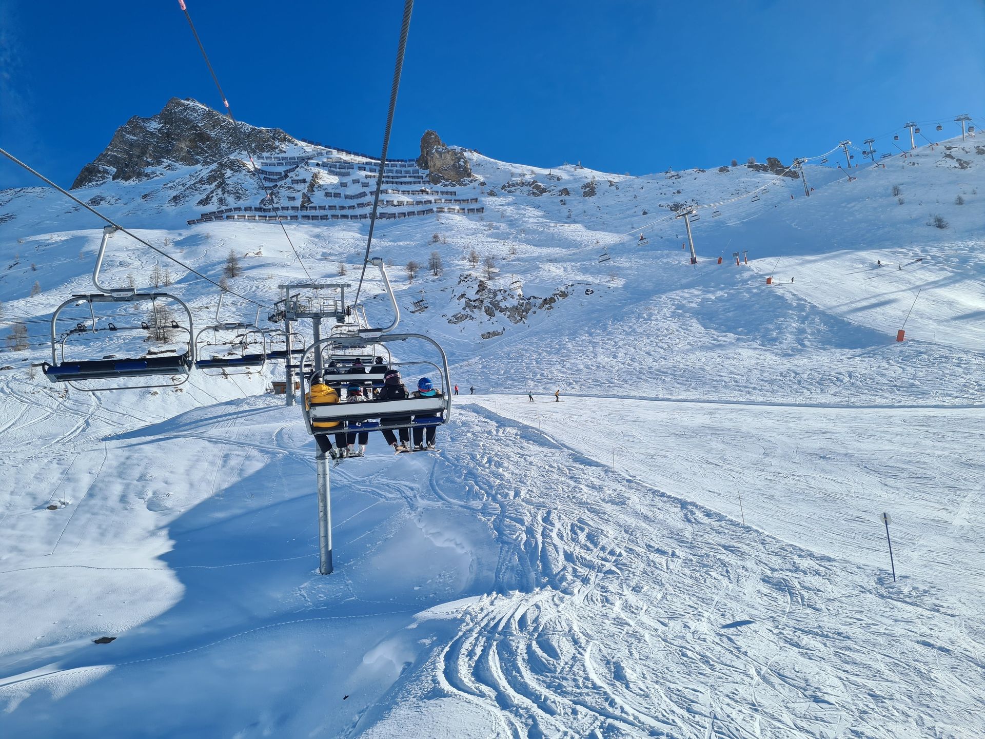 Ski lift chairs over a snowy mountain slope under a clear blue sky