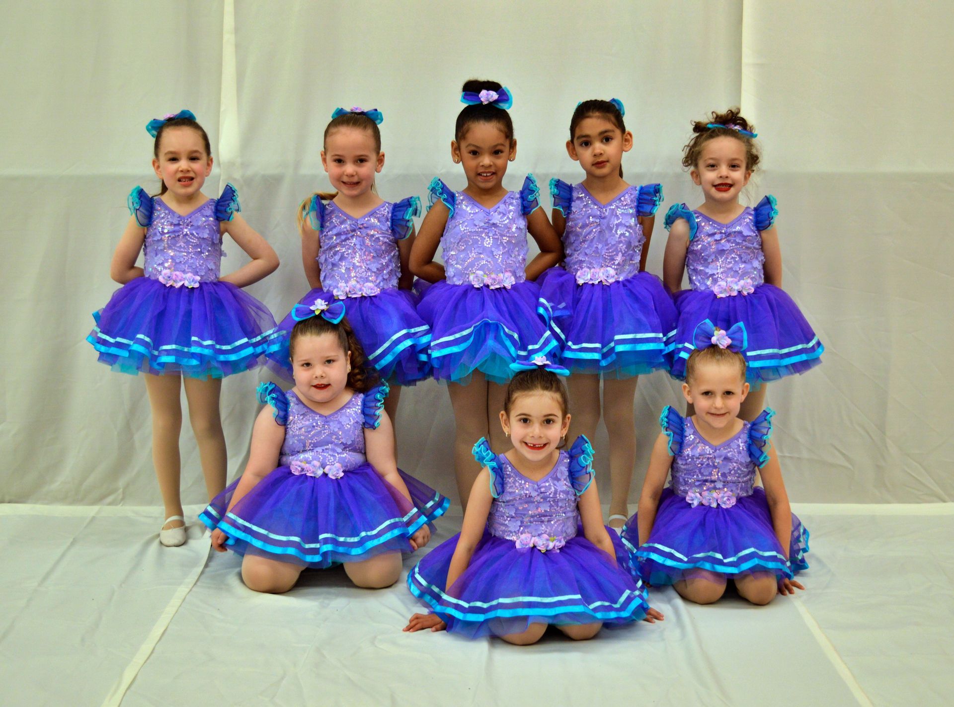 A group of young girls in purple and blue dresses are posing for a picture