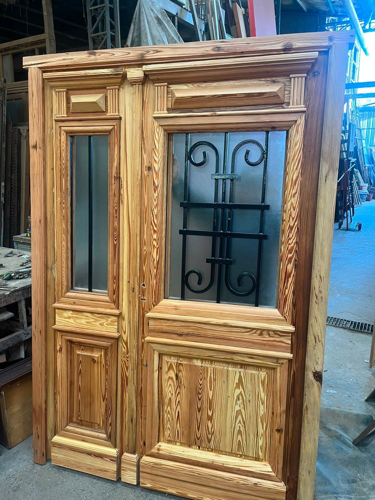 En un taller, se encuentra un mueble de madera con puerta de cristal y detalles de paneles tallados.