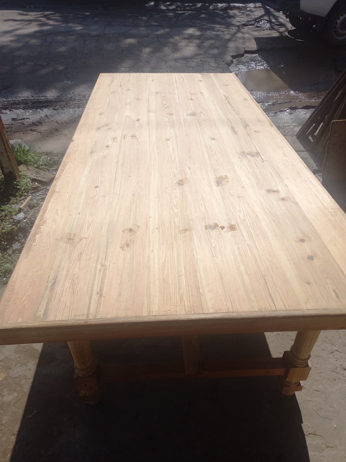 Mesa rectangular de madera clara al aire libre sobre una superficie de hormigón iluminada por el sol.