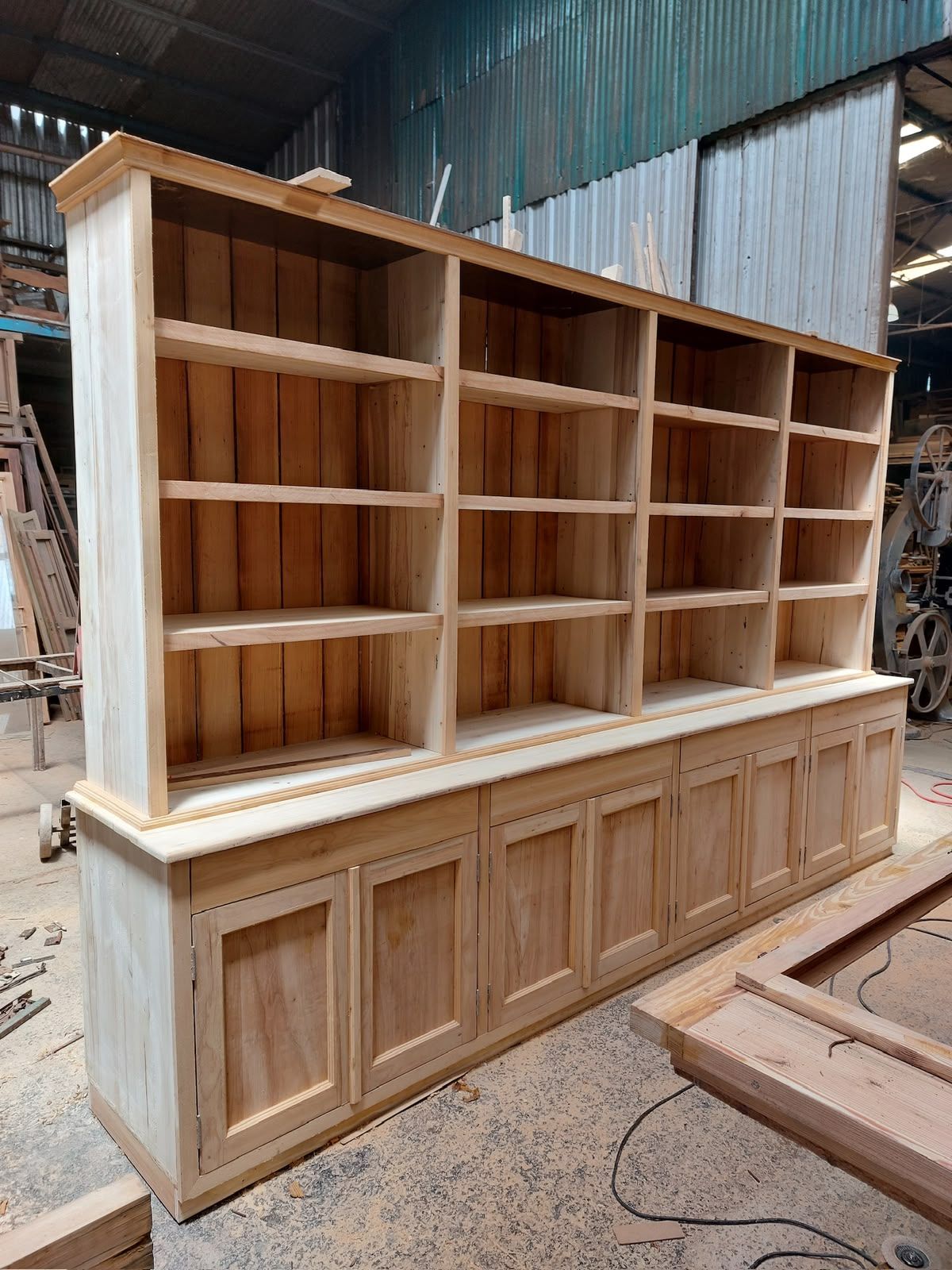 Vitrina de madera con estantes abiertos y base revestida de paneles en un taller.