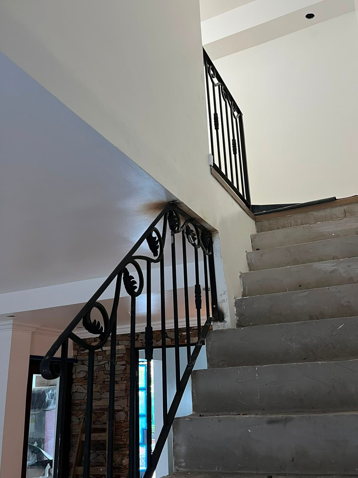 Escalera con moqueta gris y barandilla de hierro forjado negro en un luminoso pasillo interior.