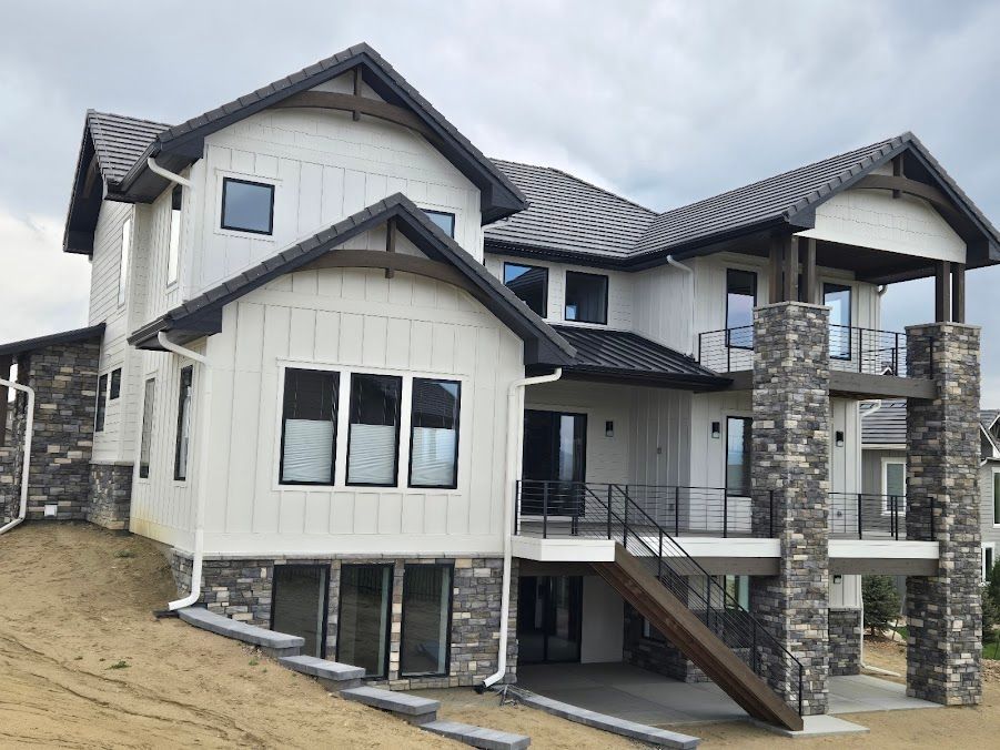Modern two-story house with stone columns, gray siding, and a partially built basement on a sloped lot