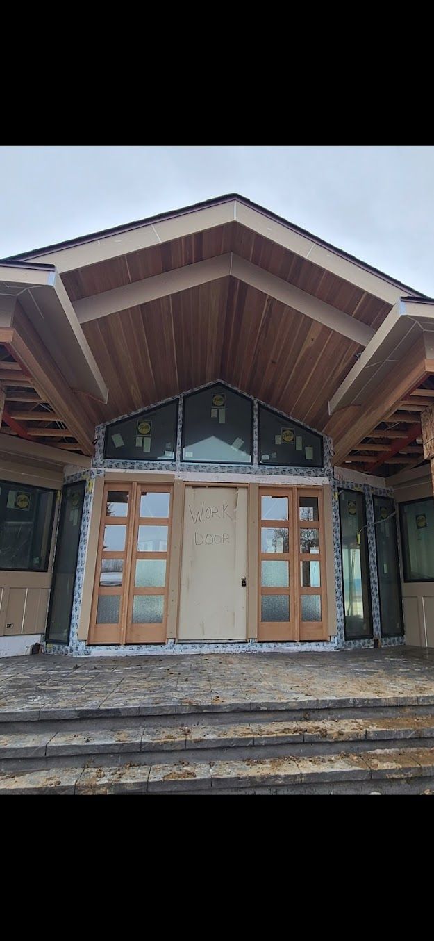 Front entrance of a rustic building with large wooden double doors and stone steps under a peaked roof.