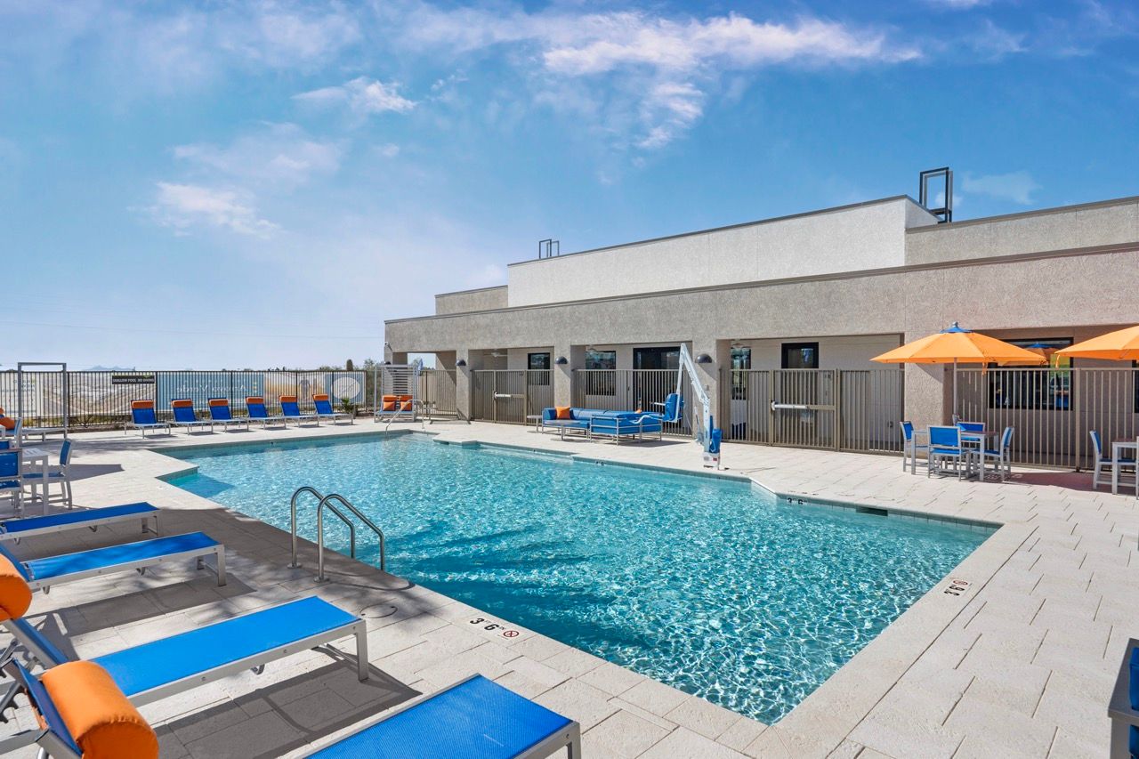 Outdoor apartment pool area with blue lounge chairs, umbrellas, and a surrounding deck.