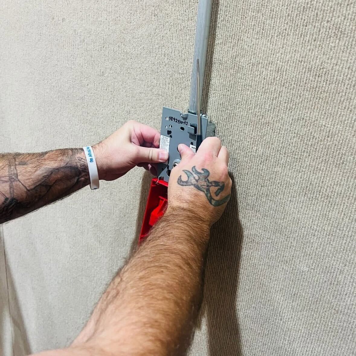 Hands fastening a gray wall-mounted device above a red object on a textured wall