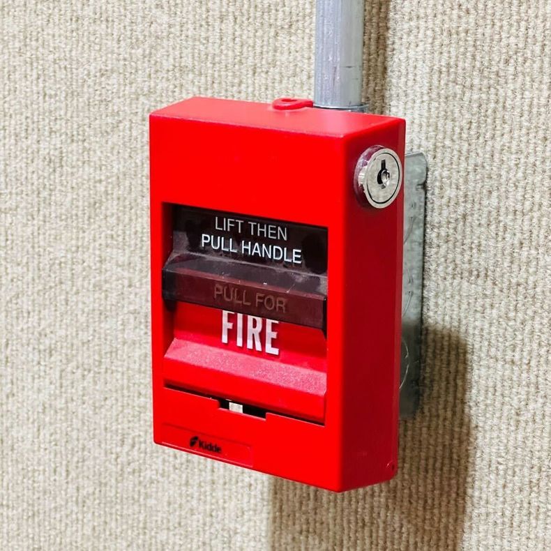 Red fire alarm pull station on a wall, with instructions to lift handle and pull for fire