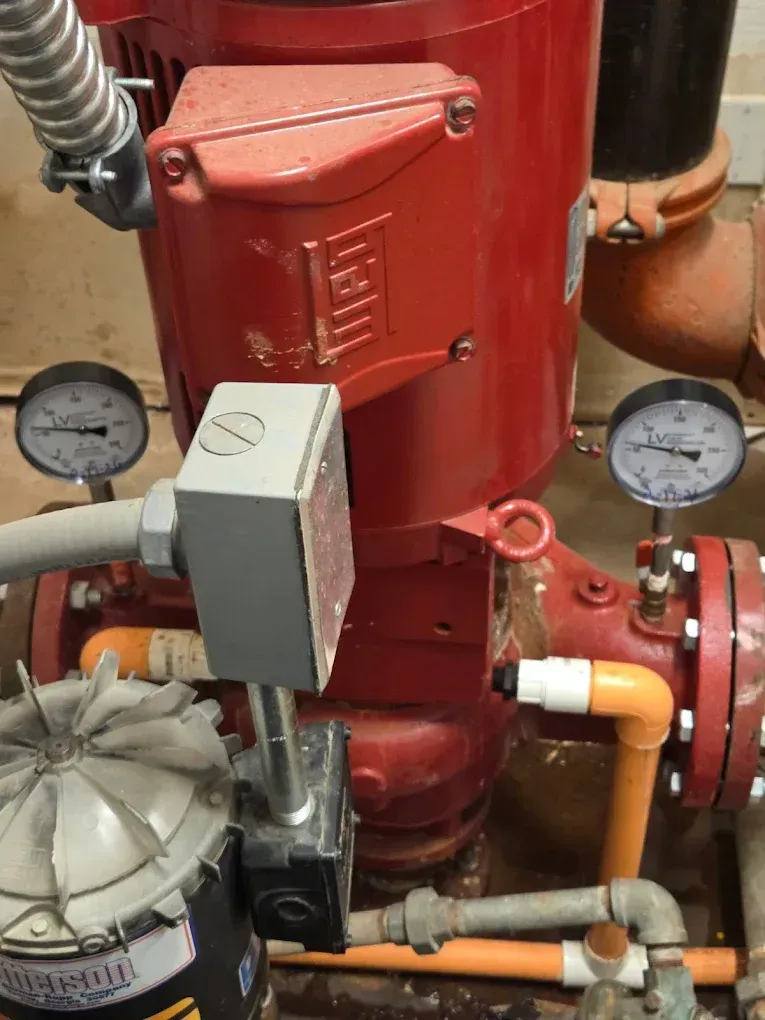 Red industrial boiler with gauges, pipes, and valves in a mechanical room