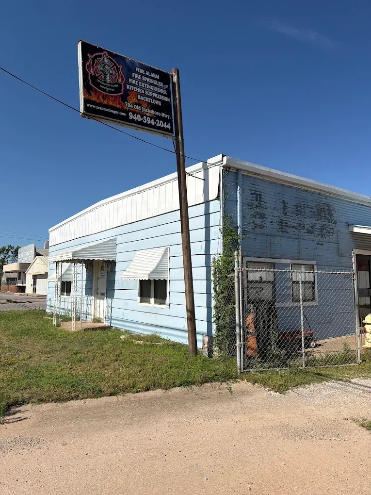 Small white building with a fenced side yard and a roadside sign under a clear blue sky