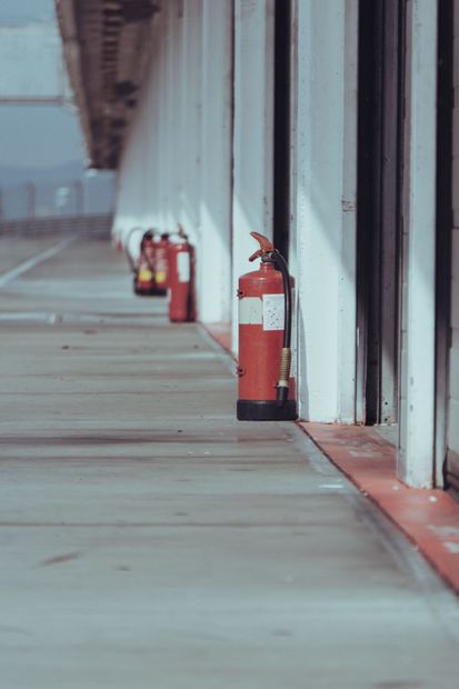 Row of red fire extinguishers along a warehouse corridor beside white walls