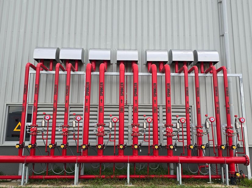 Row of red industrial sprayer booms and hoses mounted on a metal rack outdoors