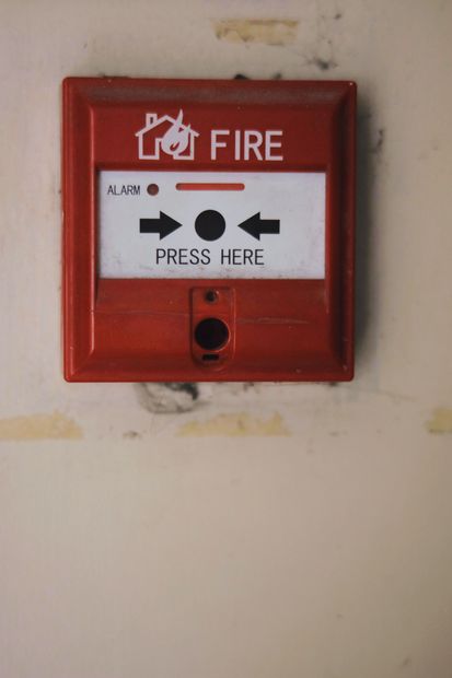 Red fire alarm call point with “PRESS HERE” label on a wall.