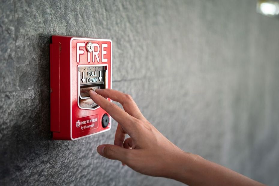 Hand pressing a red fire alarm pull station on a wall