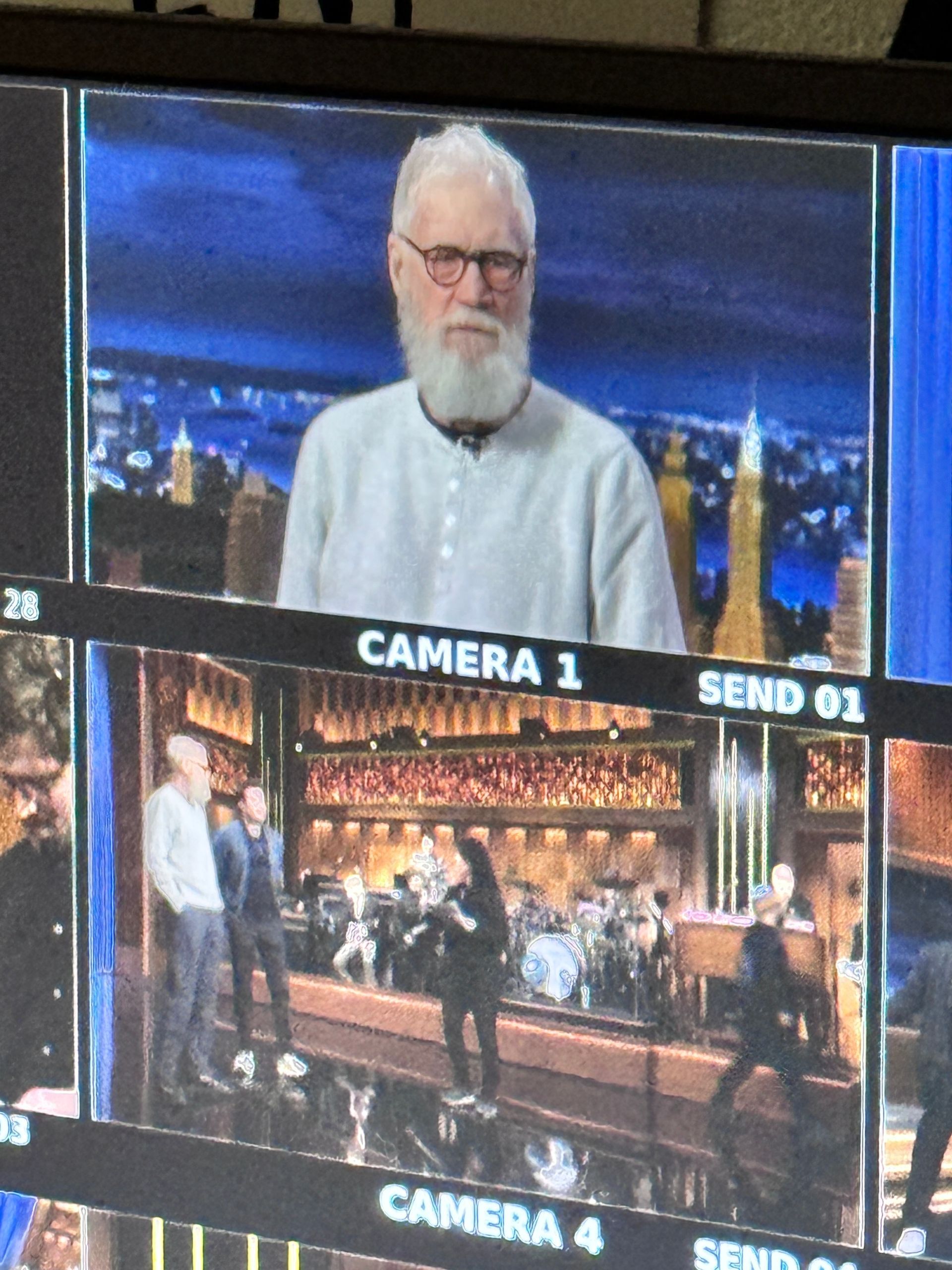 David Letterman on a monitor, with cityscape background. Below, a band performs on a stage.