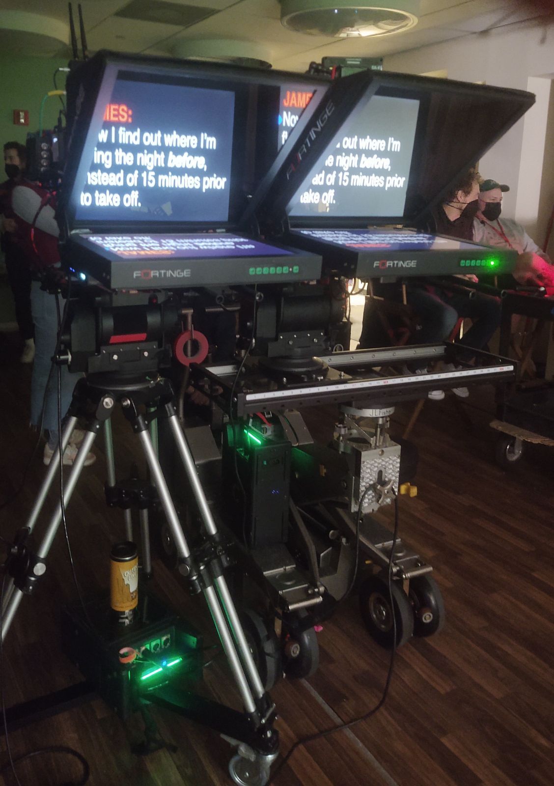 Two teleprompters mounted on tripods, likely in a studio. Each displays text for a speaker.