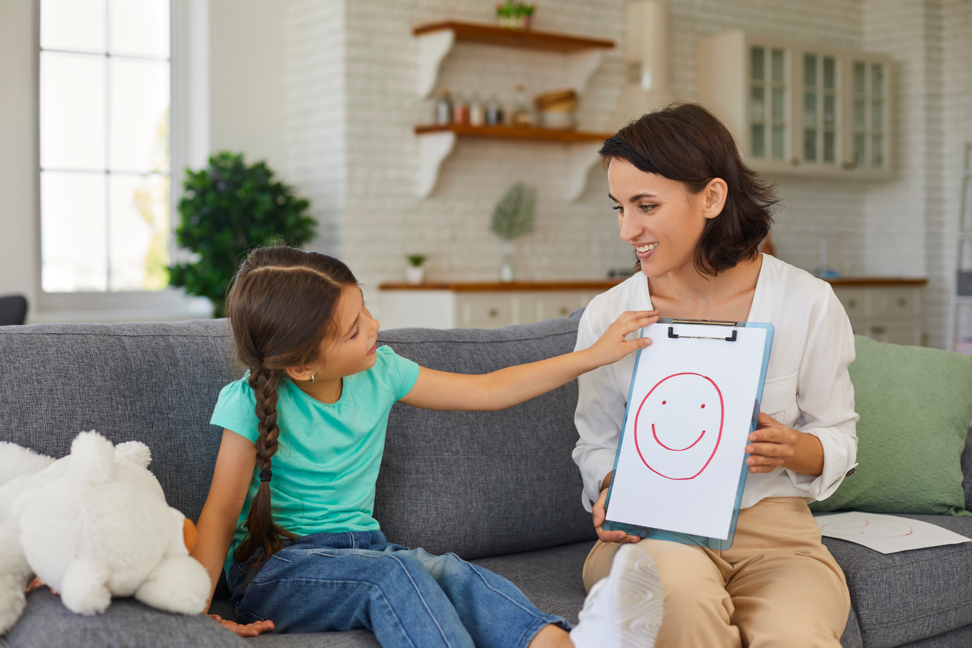 Un enfant souriant montrant un dessin à une femme assise sur un canapé dans un cadre familial.