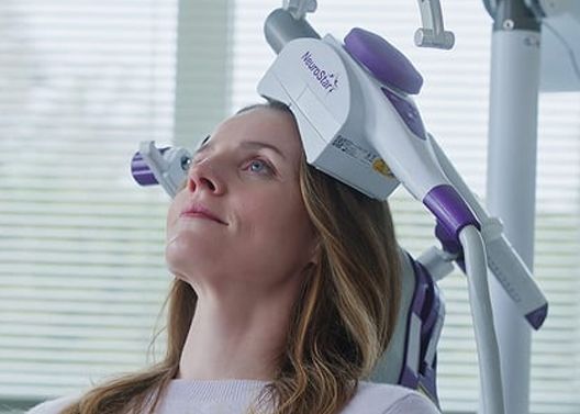 Woman with head in transcranial magnetic stimulation device.