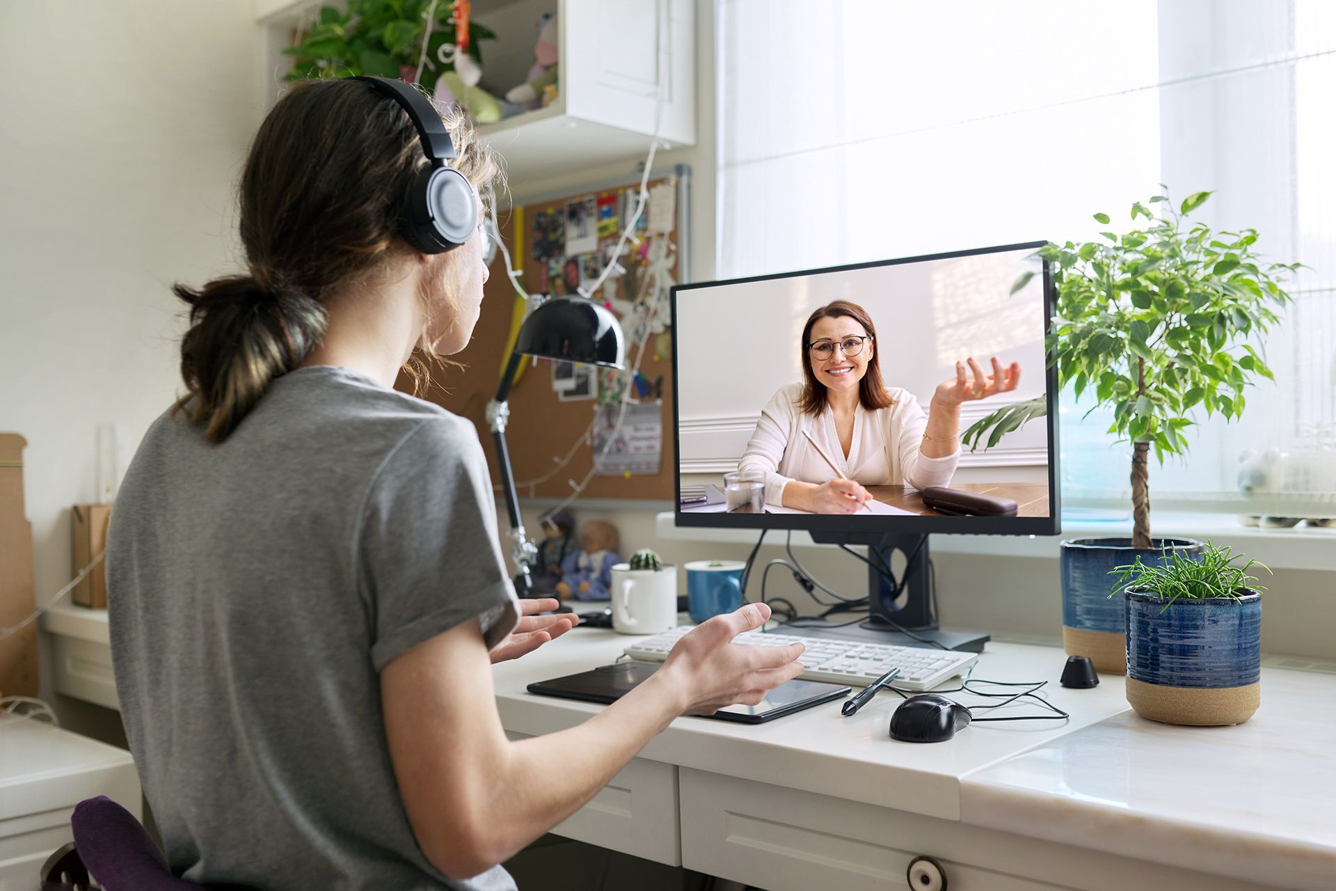 A person wearing headphones on a video call with a smiling woman, sitting at a desk in a well-lit room.