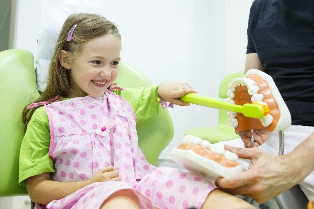 A Little Girl is Sitting in a Dental Chair Brushing Her Teeth — Tweed Banora Dental In Tweed Heads South, NSW