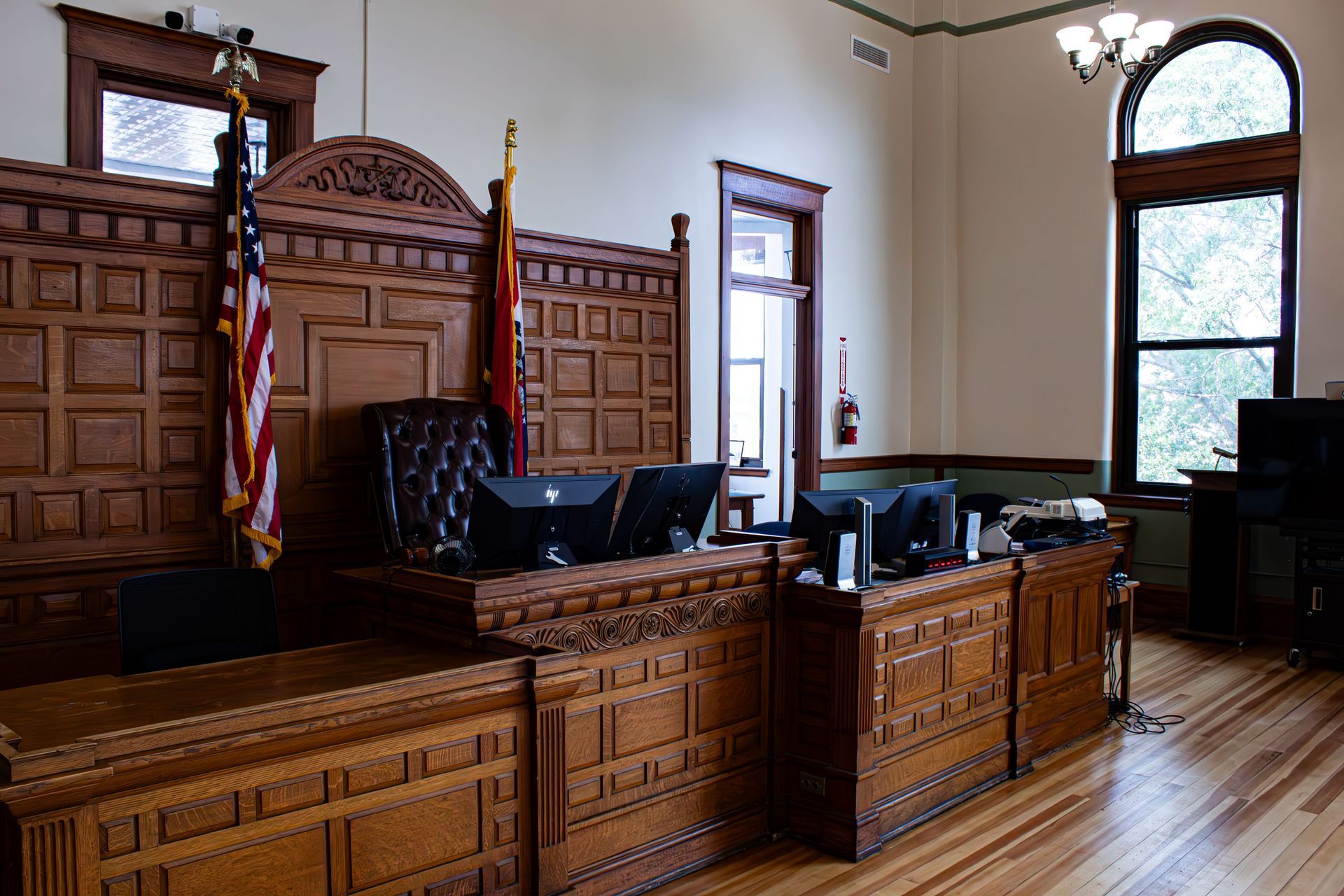 Wood-paneled courtroom with judge’s bench, American flag, and large arched windows