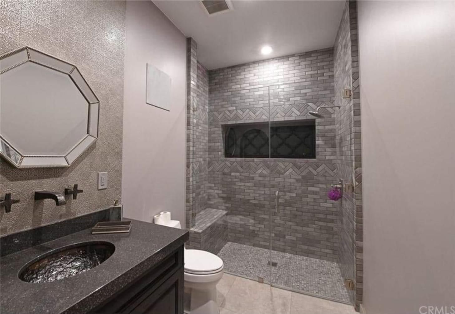 A bathroom with a toilet , sink , mirror and walk in shower.