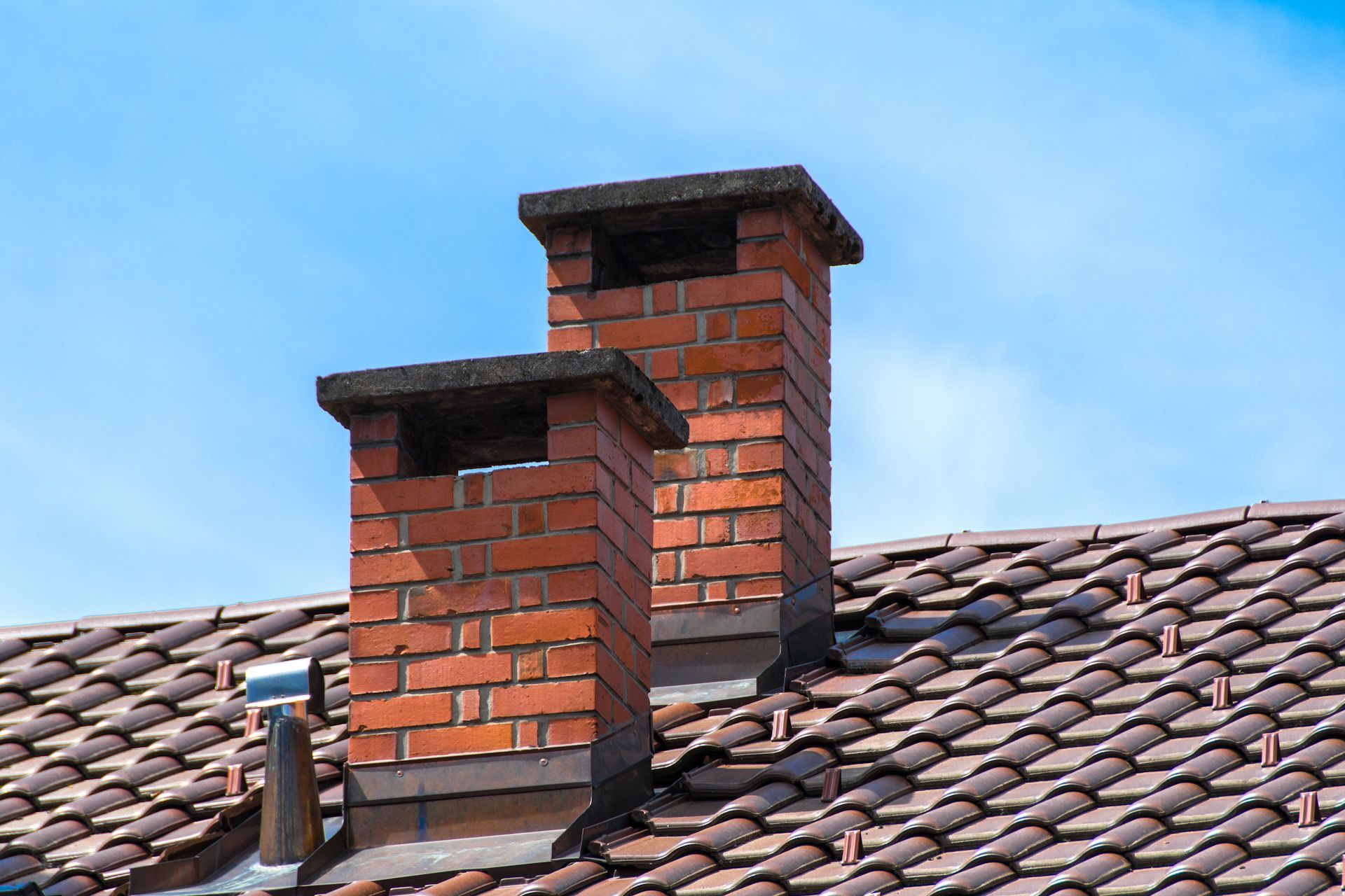 Two brick chimneys on top of a tiled roof.