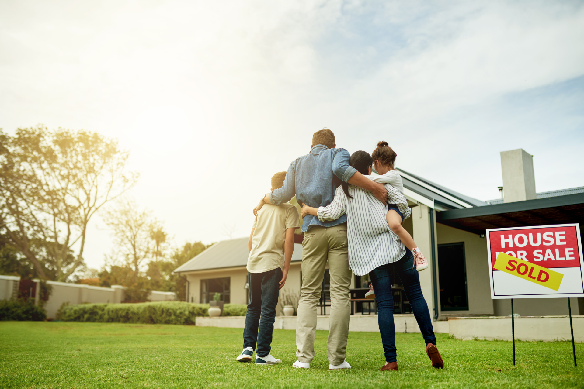 Group of people celebrating outside a house for sale with a red “SOLD” sign on the lawn.
