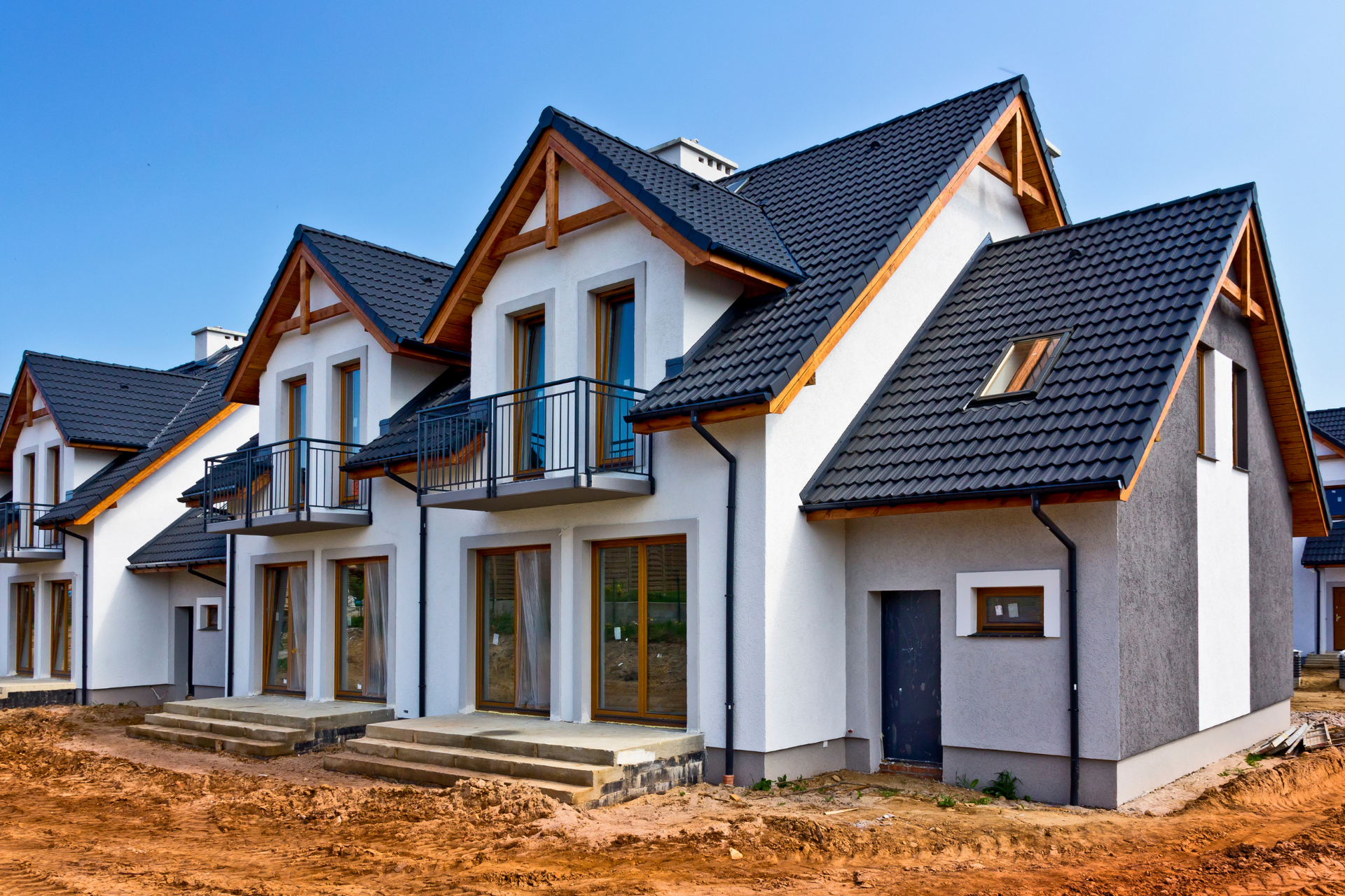 Row of modern white houses with dark blue roofs under construction on a dirt lot