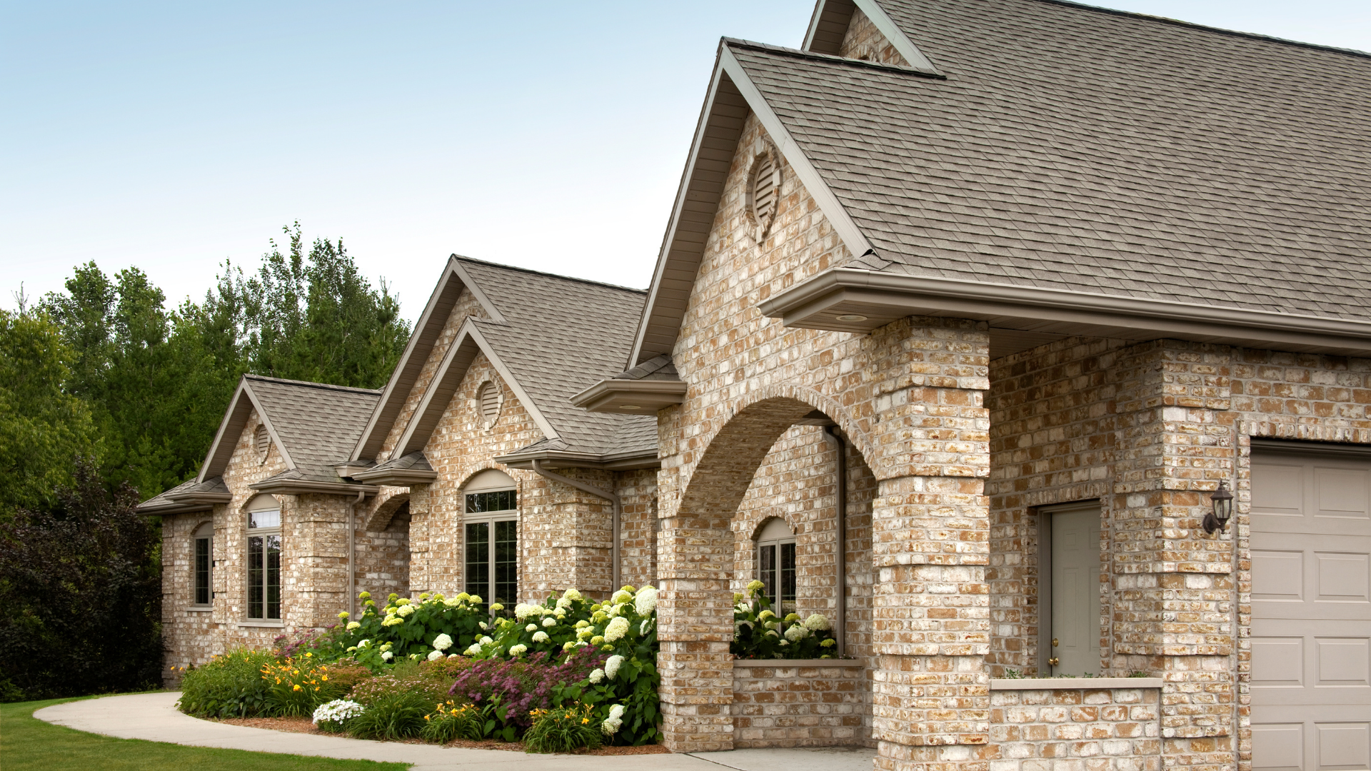 Stone houses with arched entryways and landscaped flower beds along a quiet residential street