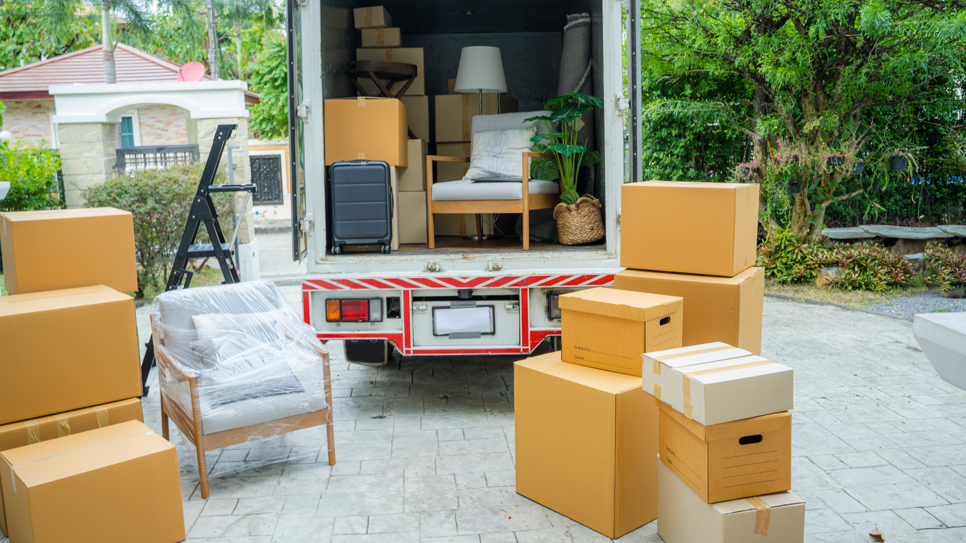 Moving truck with stacked cardboard boxes and furniture in a driveway, ready for unloading.