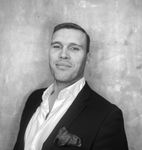 A man in a suit and white shirt is standing in front of a wall.