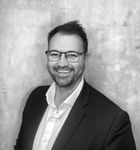A man in a suit and glasses is smiling in a black and white photo.