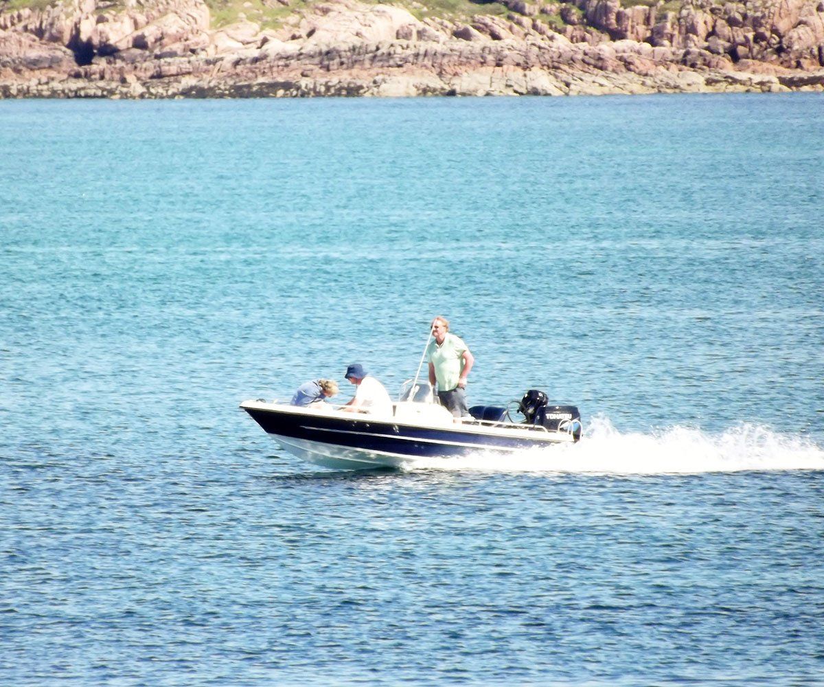 Boat with three people on blue water, coastline in the background.