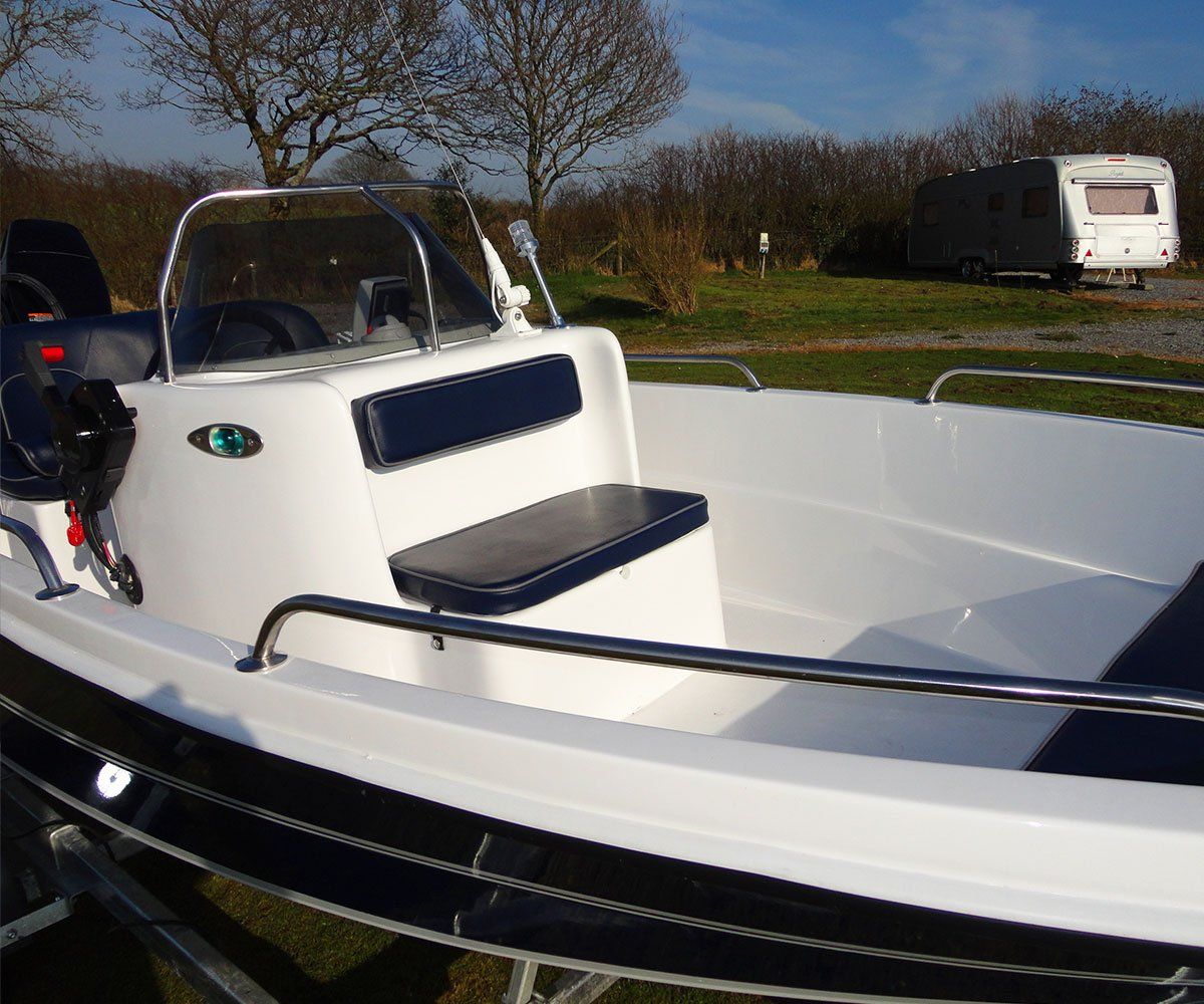 White motorboat with blue seats, parked outdoors near a grassy area and a trailer.