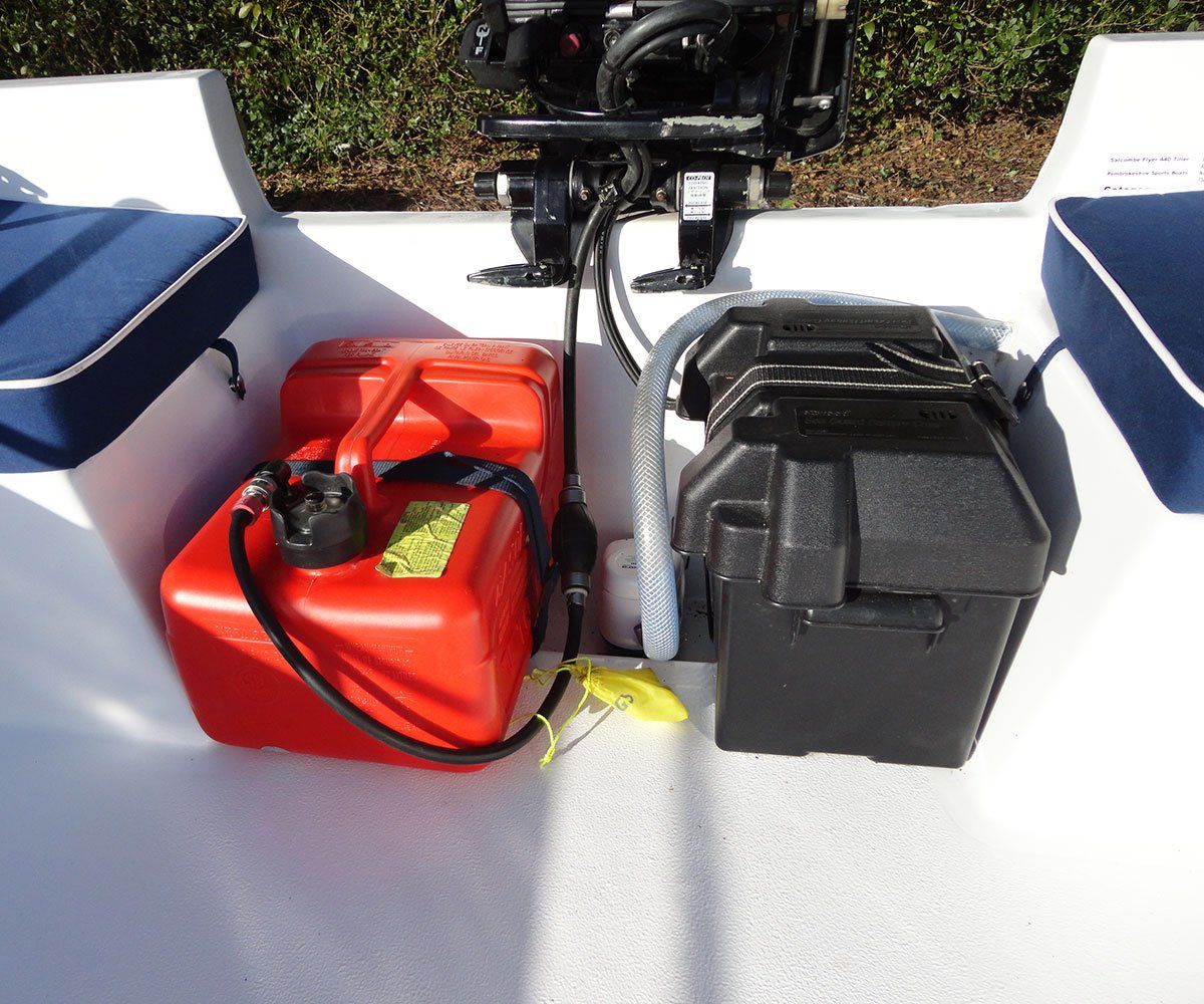 Red fuel tank and black battery box in a small boat, next to an outboard motor.