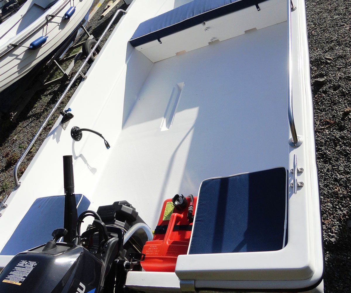White motorboat interior with engine, fuel tank, and two blue seat cushions.