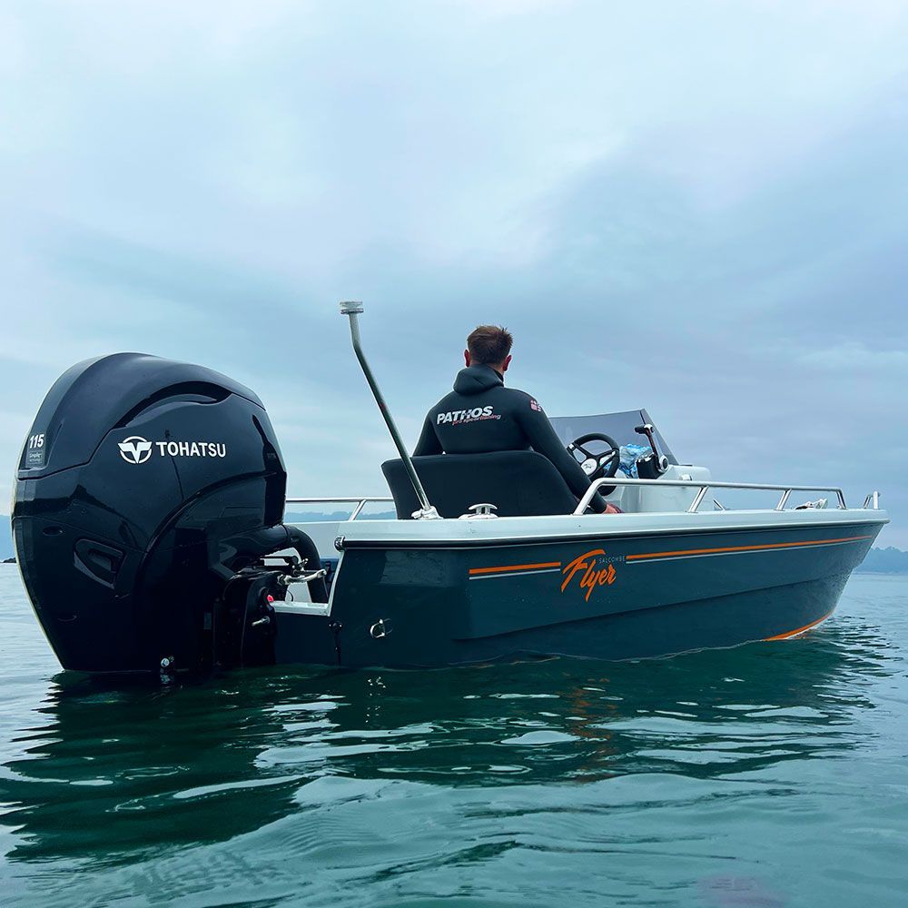 A person piloting a small black motorboat on calm water. The boat has an outboard motor. Cloudy sky.