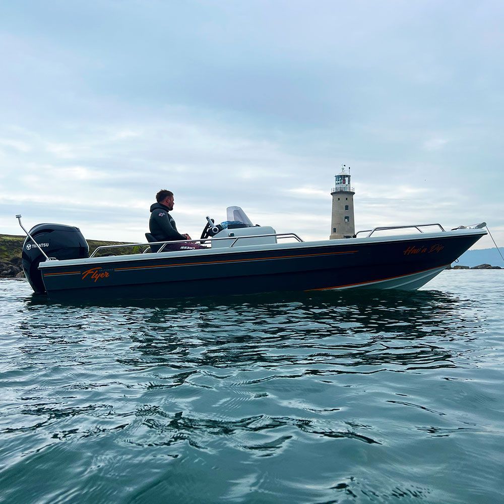 Boat on water with a person, lighthouse in background, overcast day.