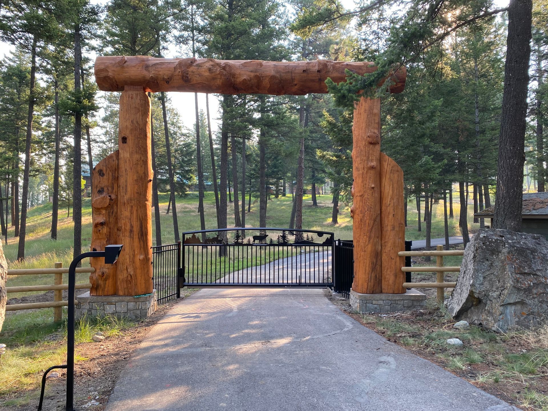 A wooden gate leading to a driveway in the middle of a forest.
