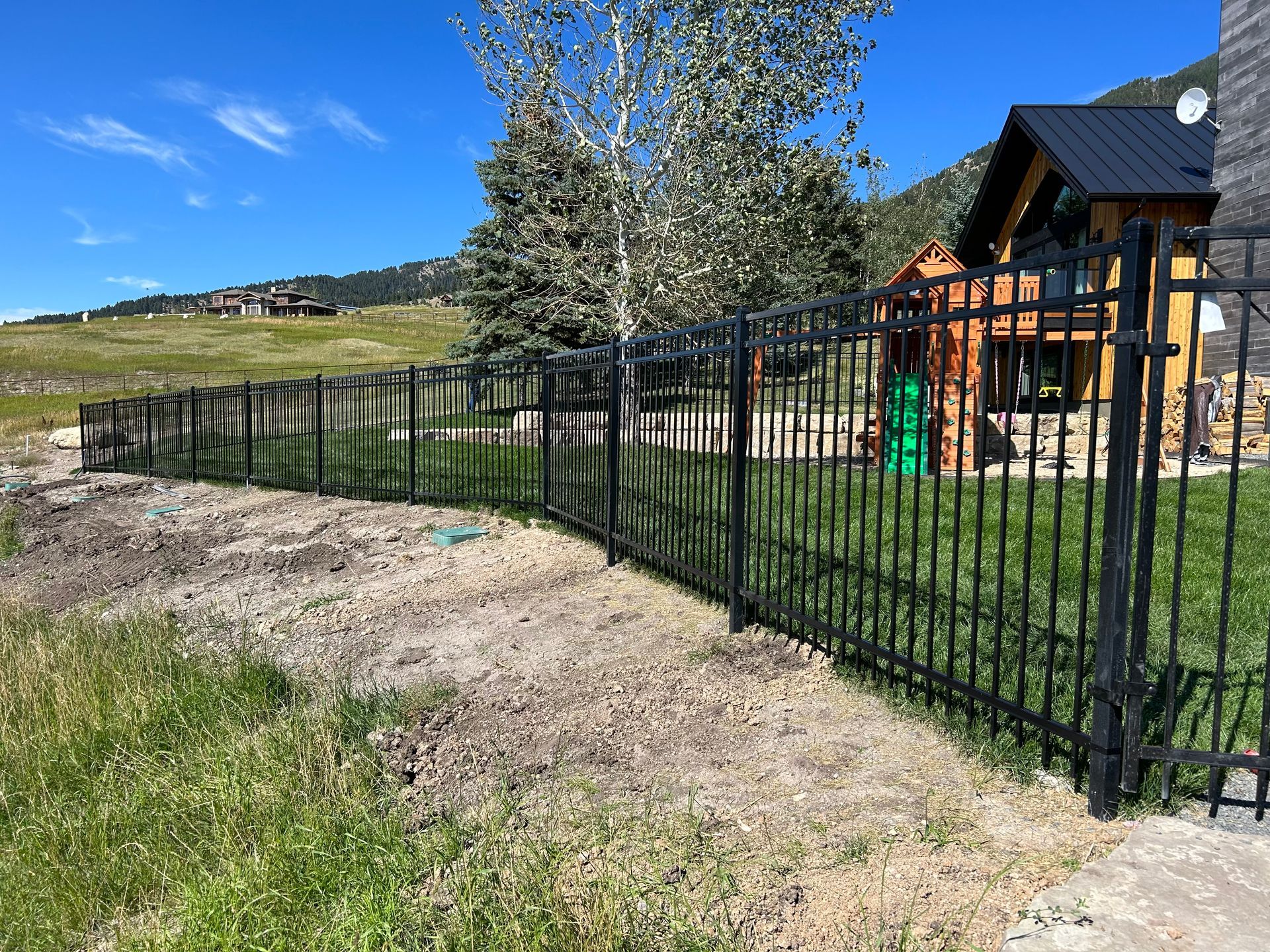 A black wrought iron fence surrounds a yard with a house in the background.