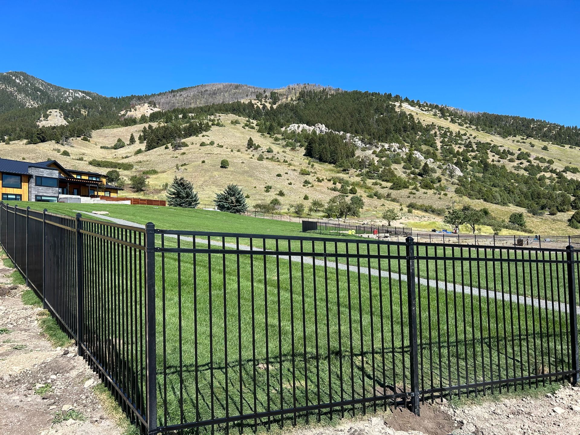 A black fence surrounds a grassy field with mountains in the background.