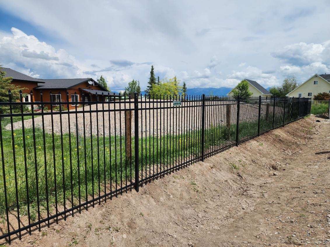 A black metal fence surrounds a yard with a house in the background.