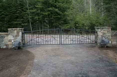 A wrought iron gate is sitting on the side of a dirt road next to a stone wall.