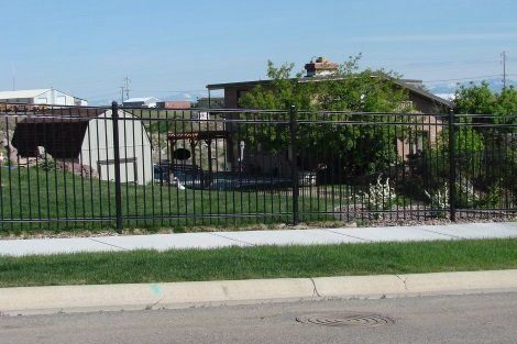 A metal fence surrounds a grassy area with a house in the background