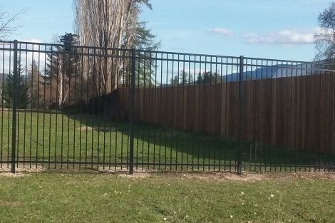 A metal fence with a wooden fence behind it in a grassy area.