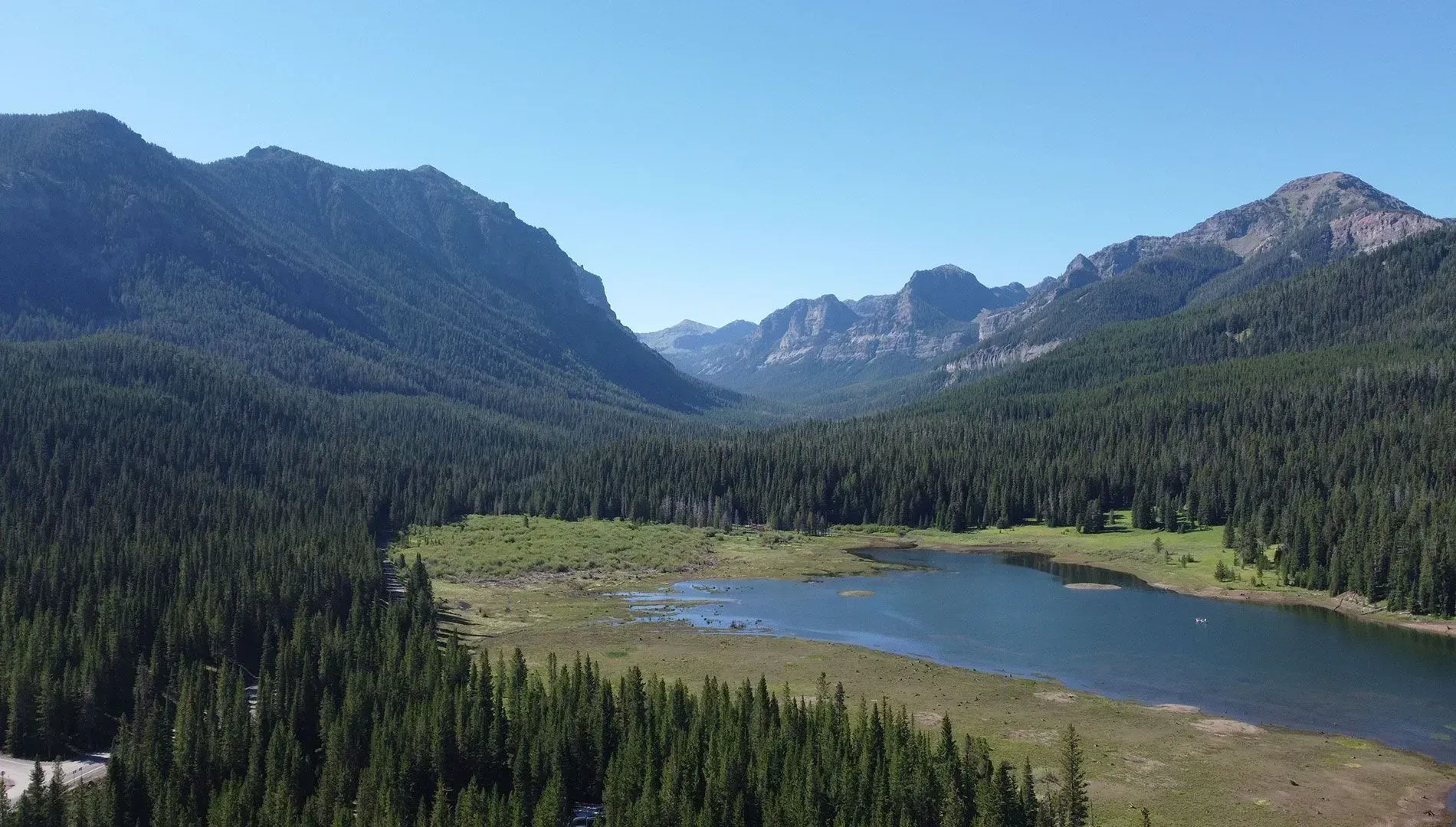 Lake surrounded by a lush green forest nestled between mountains under a clear blue sky.