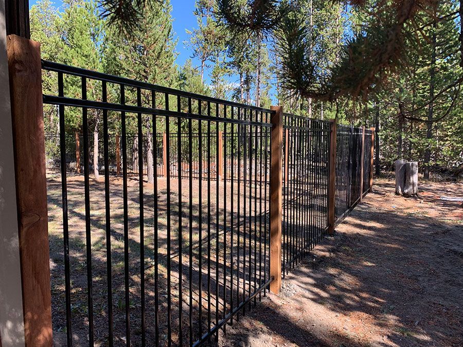 A black metal fence with a wooden post in the middle of a forest.